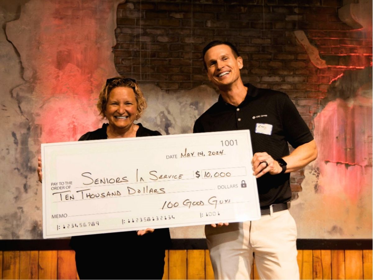 Seniors in Service CEO Robin Ingles smiling with representative from 100 Good Guys St. Pete receiving check at check presentation.
