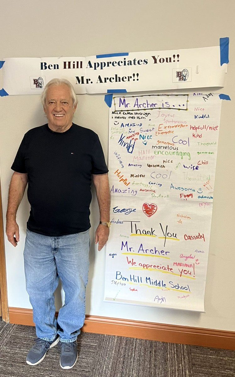 RSVP volunteer Jim Archer stands beside a student-made appreciation banner at Ben Hill Middle School recognizing his dedication to mentoring and supporting students.