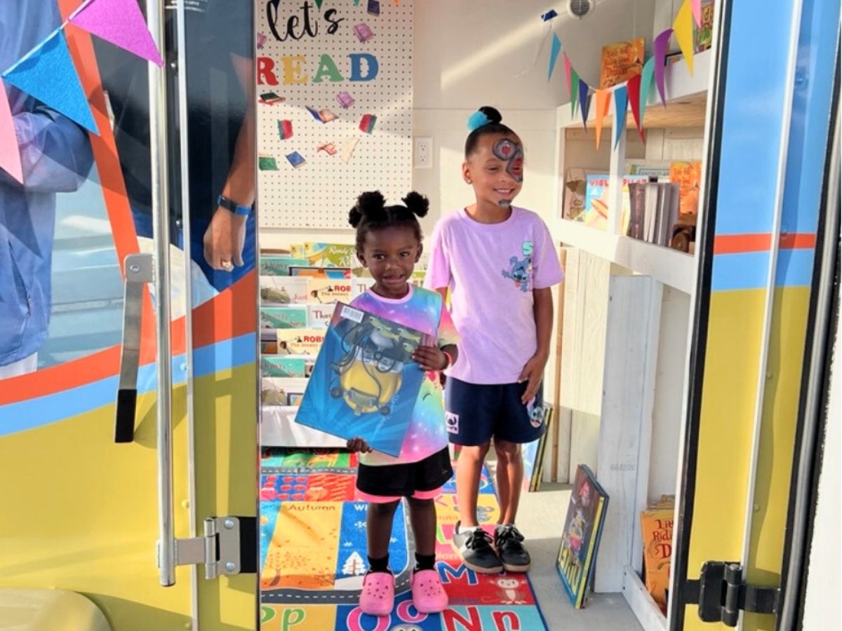 Two children proudly hold their new books inside the Seniors in Service mobile book trailer during a community literacy event.
