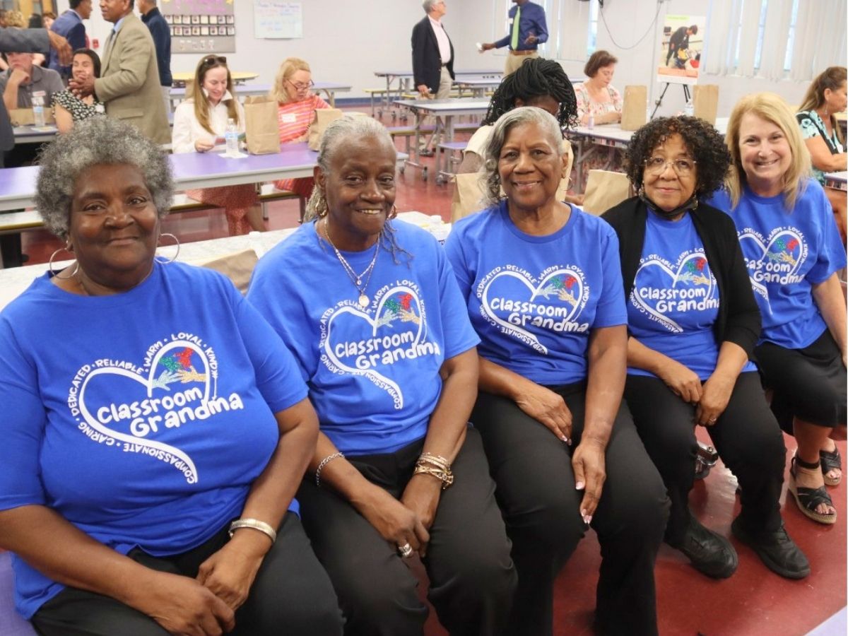 Classroom grandparents pose for a picture together, wearing Classroom Grandma t-shirts.