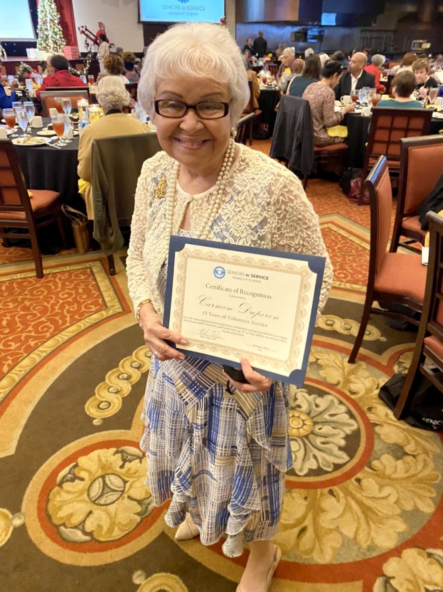 Classroom Grandparent volunteer holds a Hero of Service award during the Annual Volunteer Appreciation Luncheon.