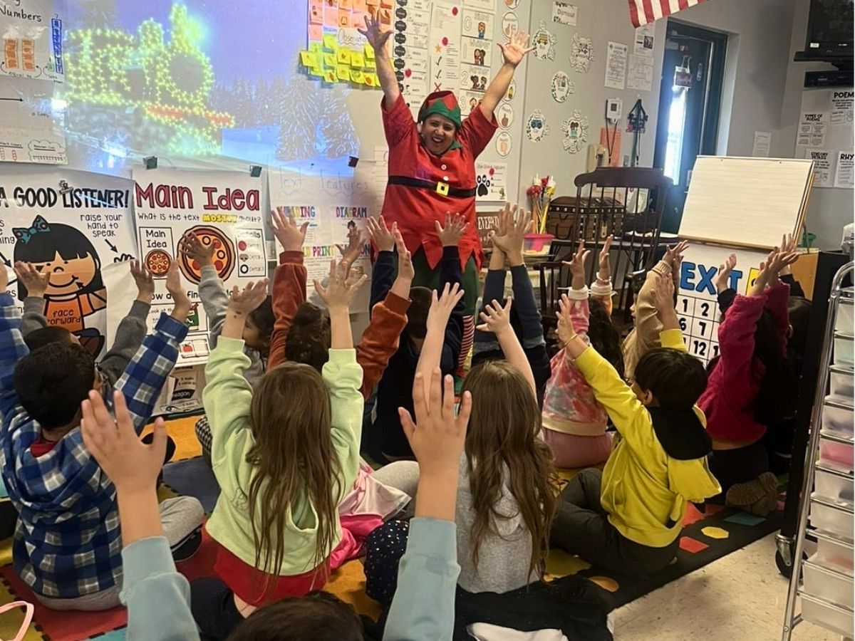 A Classroom Grandparent leads an interactive holiday learning activity as elementary students eagerly raise their hands during a Readers in Motion classroom lesson.