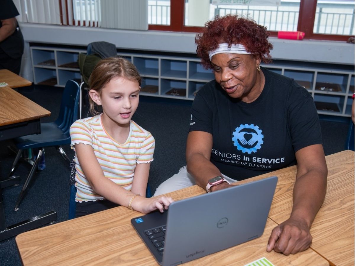 Classroom Grandparent volunteer tutors a student using a computer to practice letter recognition and phonics skills.