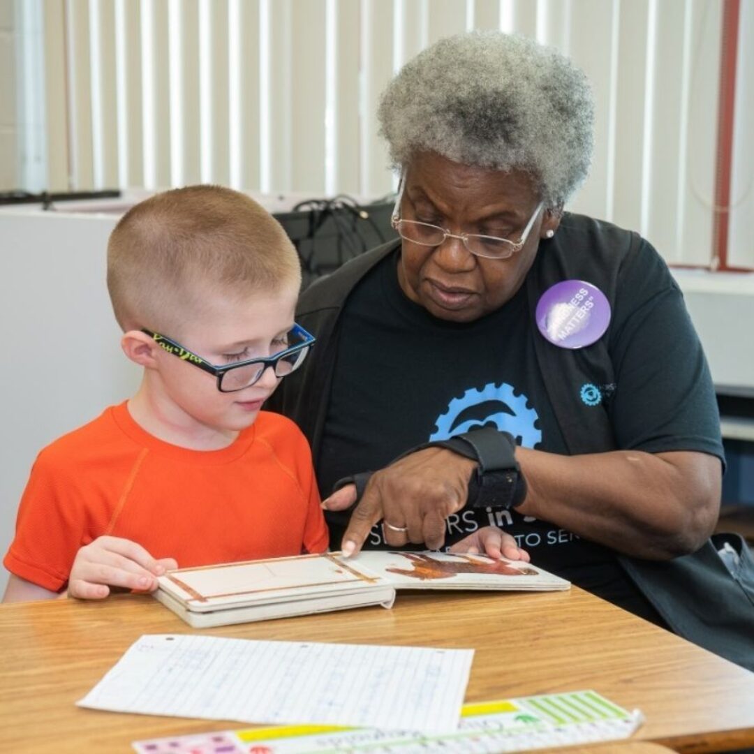 Seniors in Service Classroom Grandparent volunteer helping student learning sight words with book.