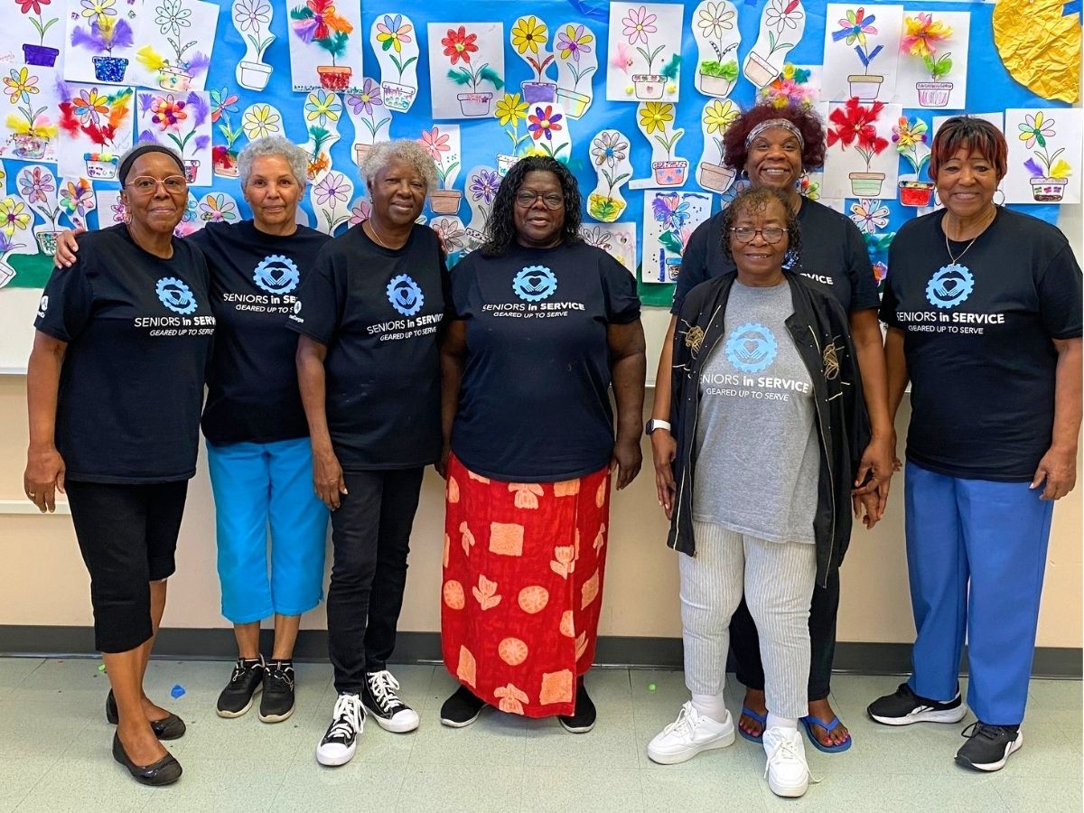 Classroom Grandparent volunteers gathered together for a group photo in front of colorful student flower artwork.