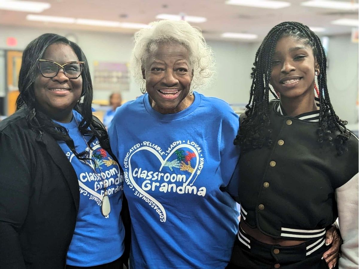 Assistant Principal Sa&rsquo;Tonya Brascom, Classroom Grandparent Grandma Woody, and student Harmoni smiling together at school.