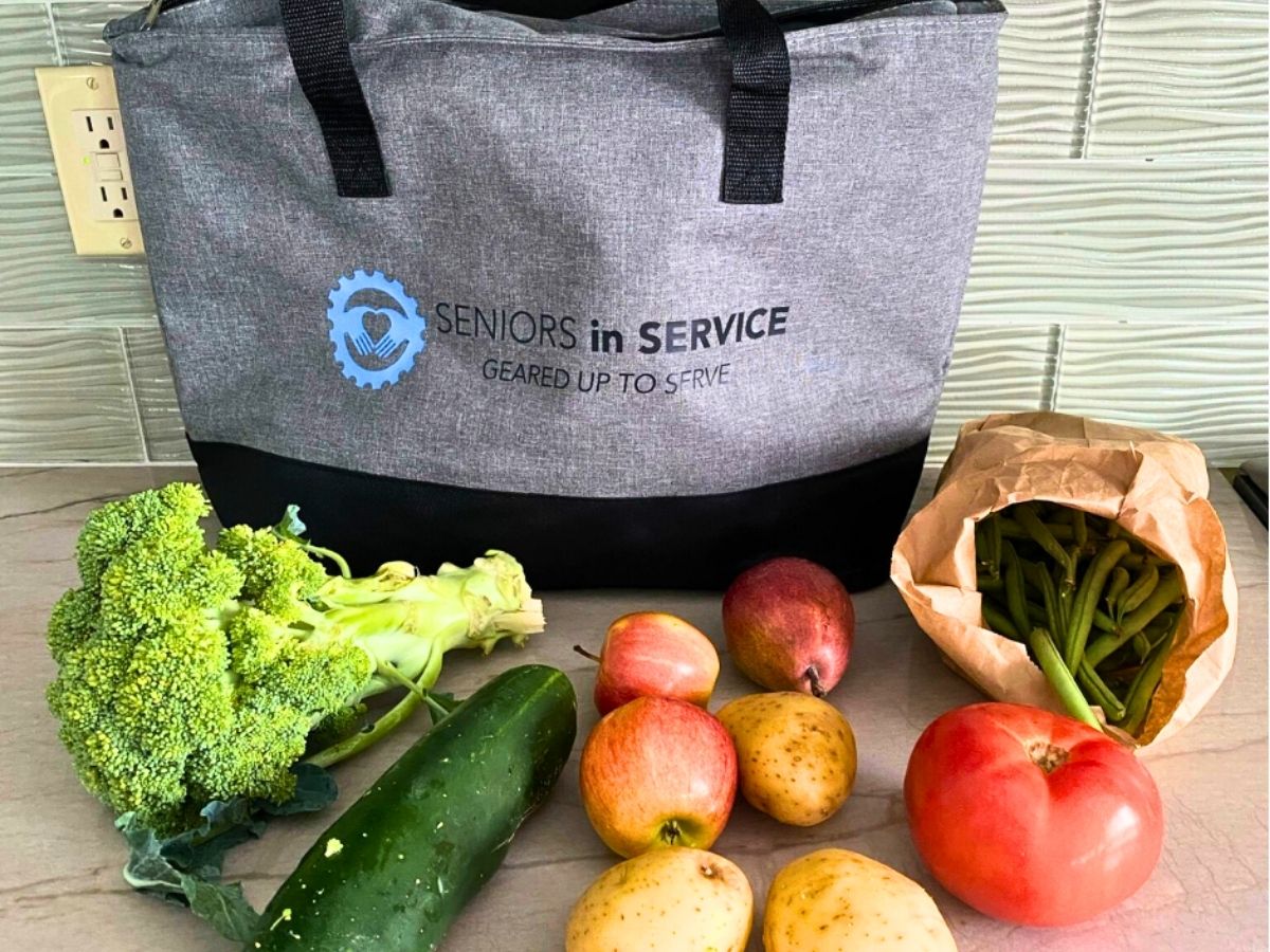Fresh fruits and vegetables displayed beside a reusable tote bag as part of the Health Buddies program's healthy food delivery initiative for older adults.
