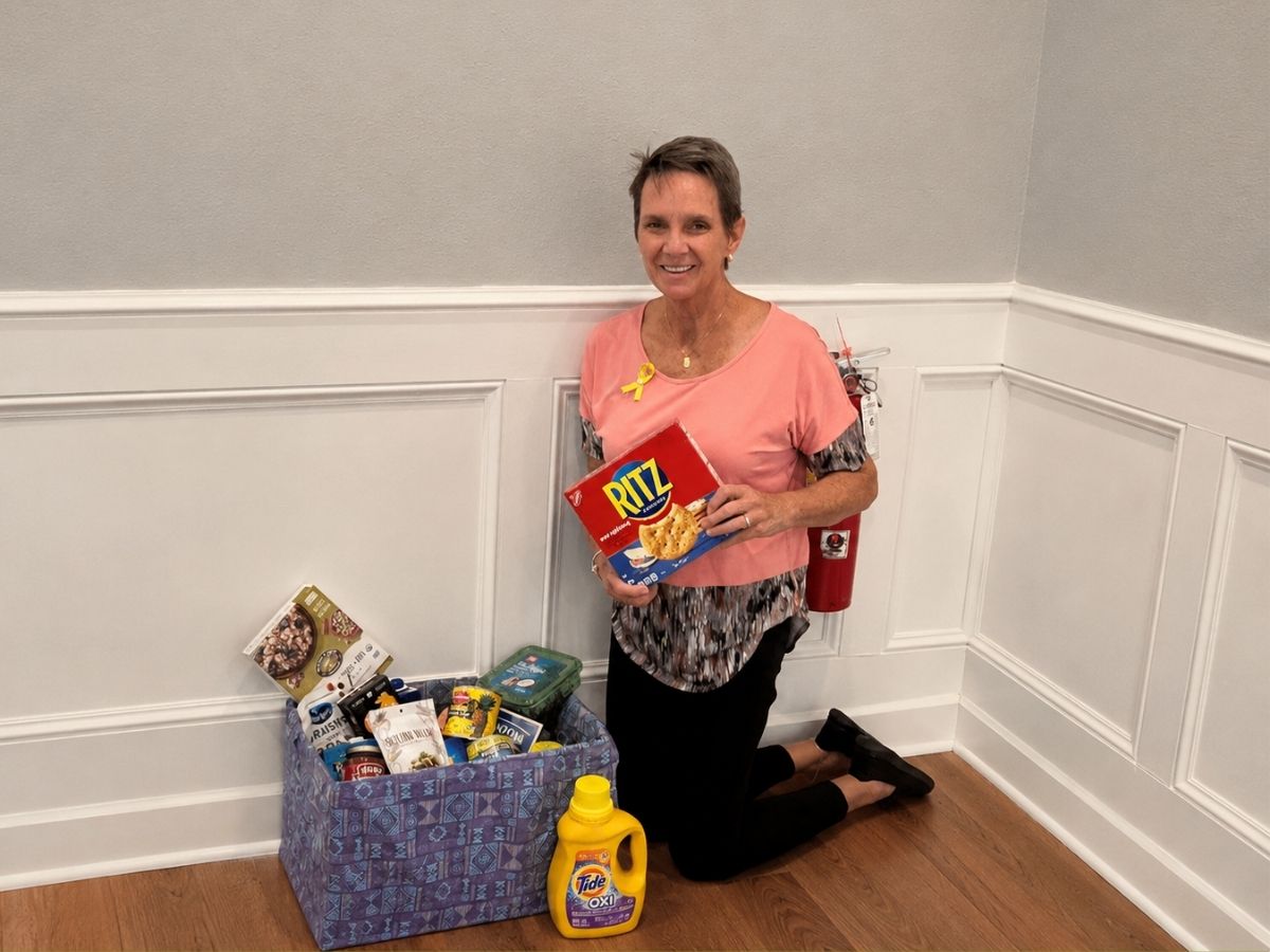 A woman kneels beside donated food items while wearing a yellow ribbon symbolizing friendship and connection through the Kindred Spirits Club.
