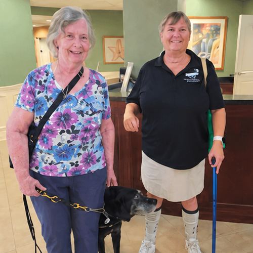 Two women stand with a guide dog during a Seniors in Service low-vision support group meeting at Lighthouse for the Blind & Low Vision.