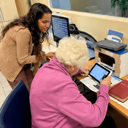 A volunteer assists an older adult using a tablet during a low-vision support group meeting at Lighthouse for the Blind & Low Vision.