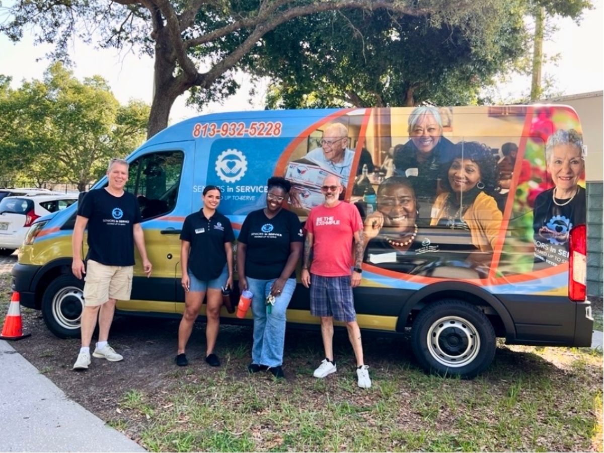 Volunteers stand beside the Seniors in Service Mobile Outreach Van during a community outreach event in Tampa Bay.