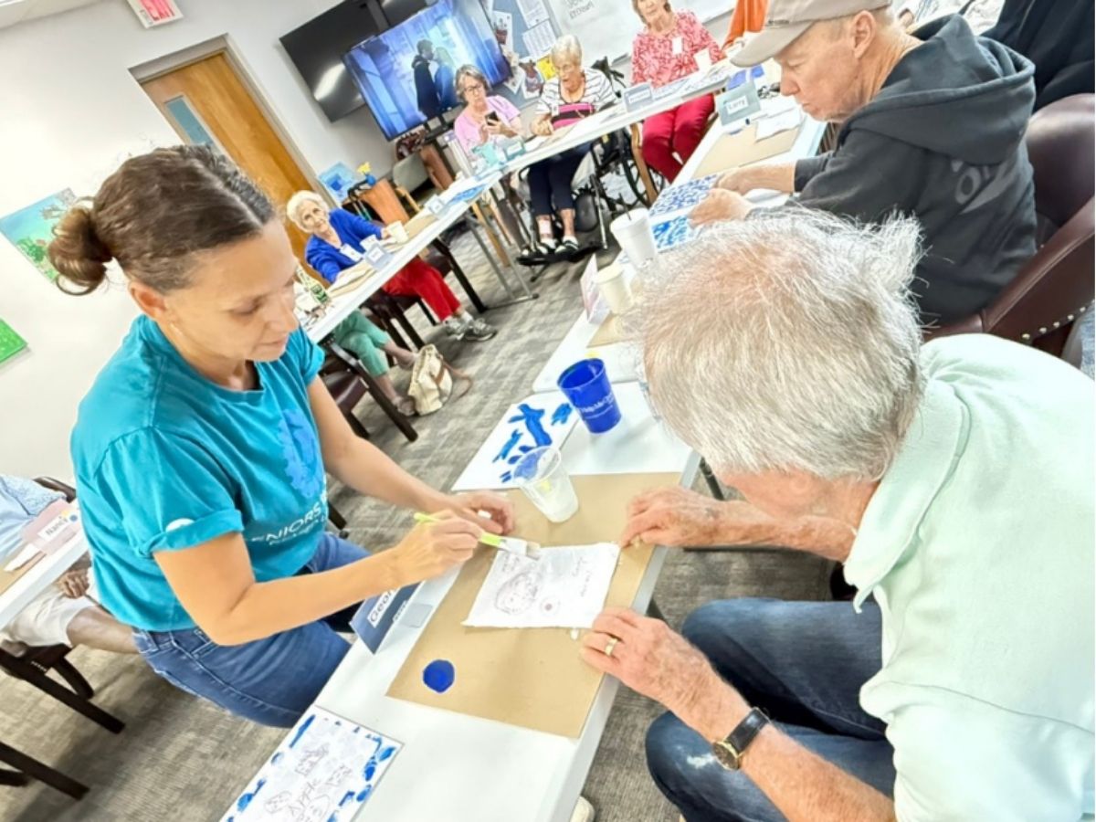 Senior Companion volunteer assists an older adult with an art activity during a dementia-friendly creative engagement program at Ruth's Promise in Pinellas County.