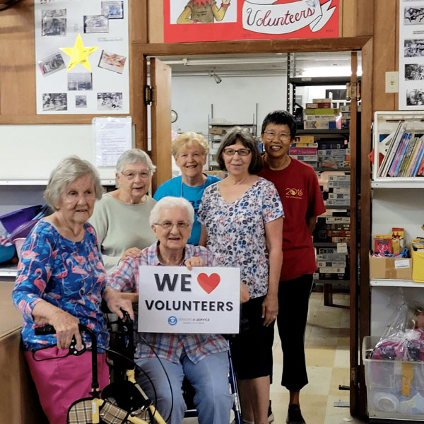 RSVP volunteers gather at a community service site holding a "We Love Volunteers" sign in recognition of their dedication to serving Tampa Bay.