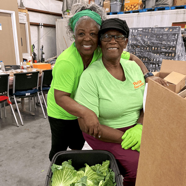 Two RSVP volunteers smile while packing fresh produce and food boxes at a Florida food pantry serving families in need.