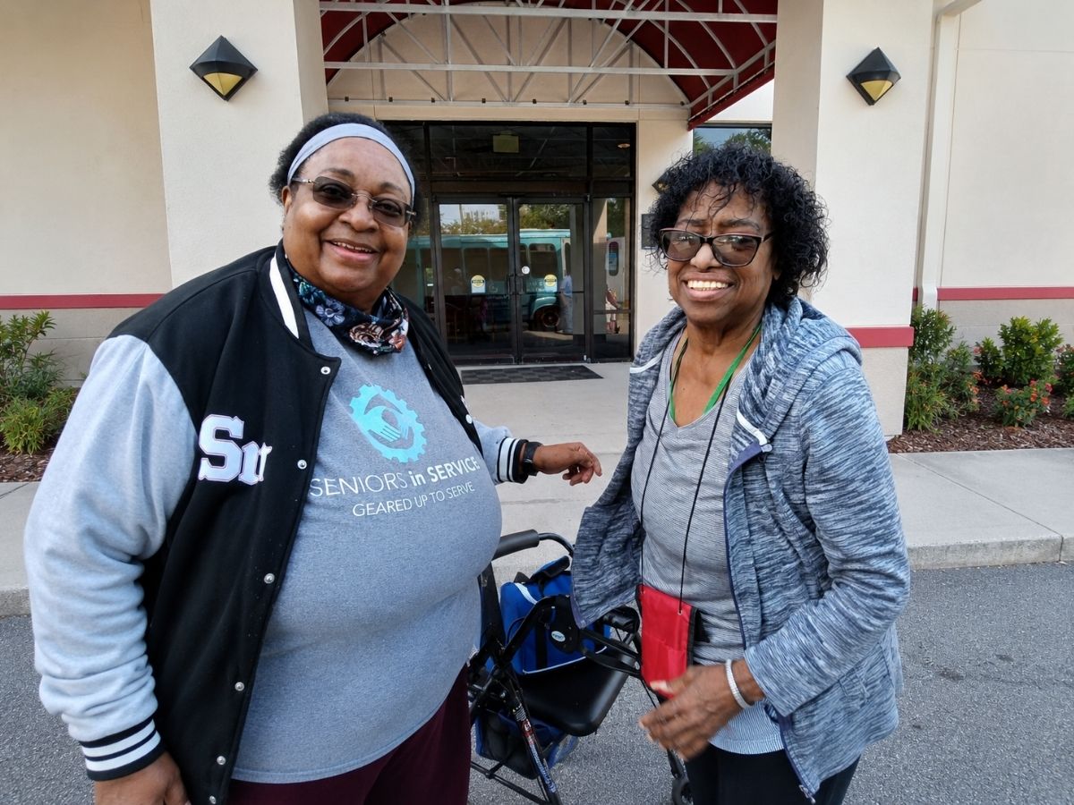 Senior Companion volunteer Lauren Smalls stands smiling with her client Shiela during a community recognition event in Pinellas County.