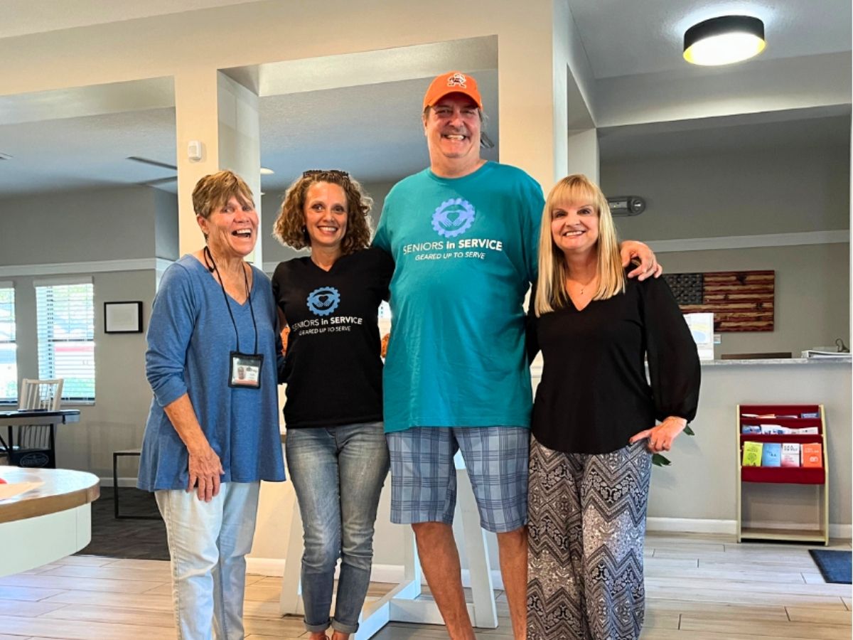 Senior Companion volunteers and staff members gather together at a community residence, celebrating companionship, friendship, and support for older adults.