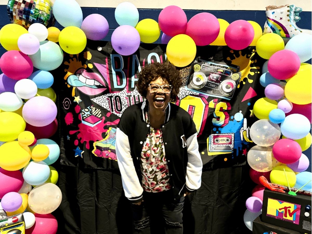 Volunteer poses in front of an 80s-themed photo booth during Seniors in Service's 40th anniversary volunteer appreciation celebration.