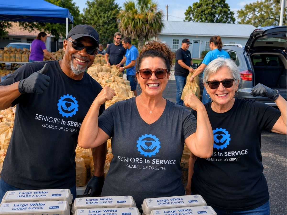 Senior volunteers and community members pose at a food distribution event while helping organize grocery bags and supplies.