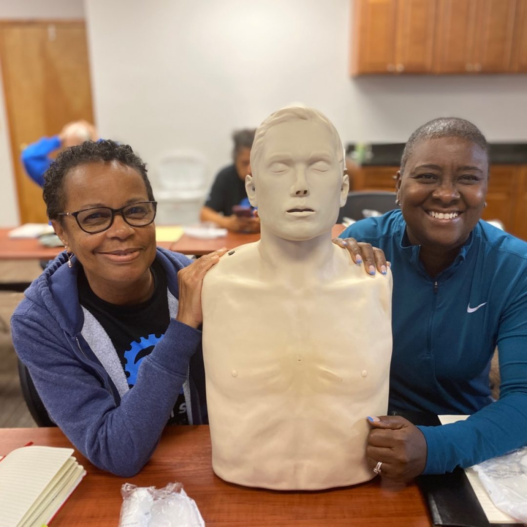 Operation: Veteran Connect members smiling with CPR dummy model during training session.