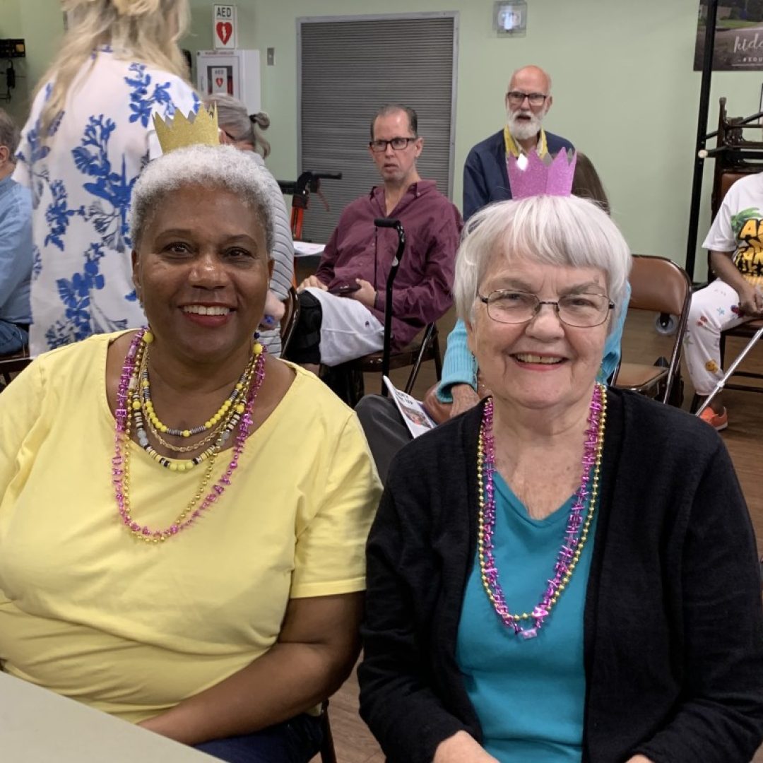 A Senior Companion volunteer and her senior companion wear matching necklaces at a community event.