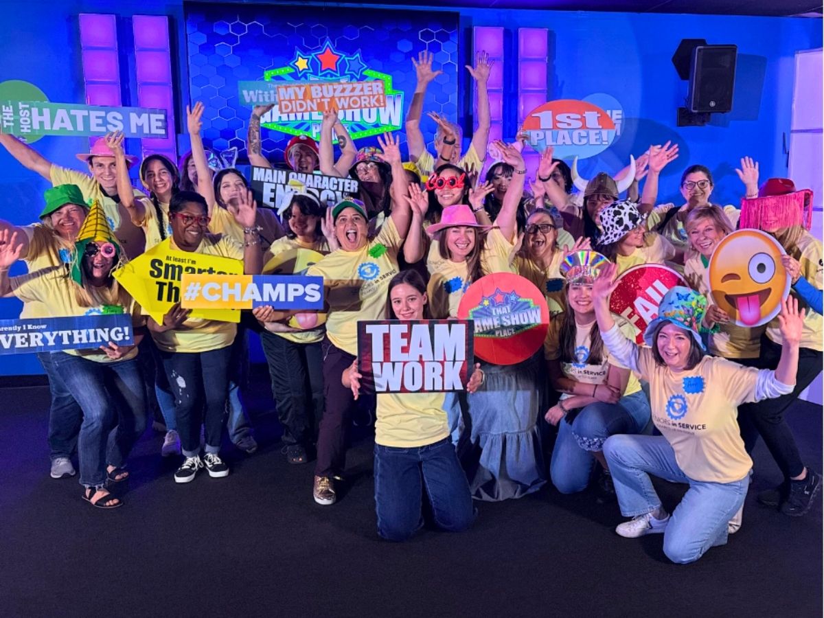 Seniors in Service staff members celebrate during a team-building game show event, holding signs and cheering together.