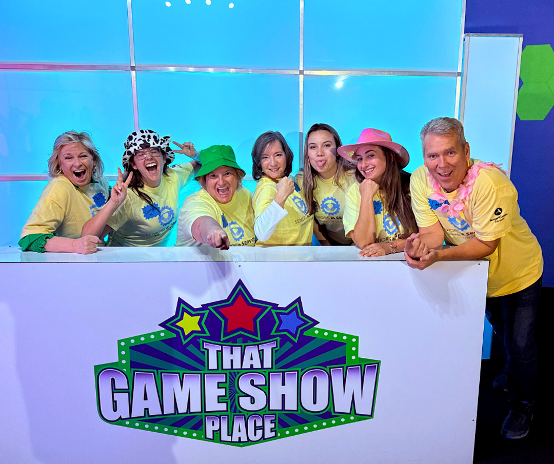 Seniors in Service staff pose together during a team-building event at a game show studio.