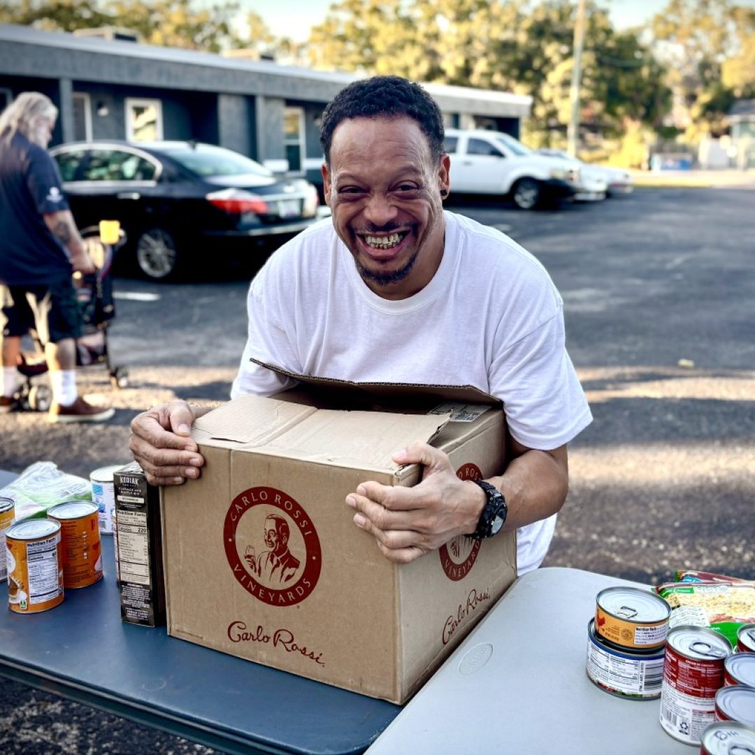 A veteran smiles while holding a box of packaged goods at a mobile food pantry.