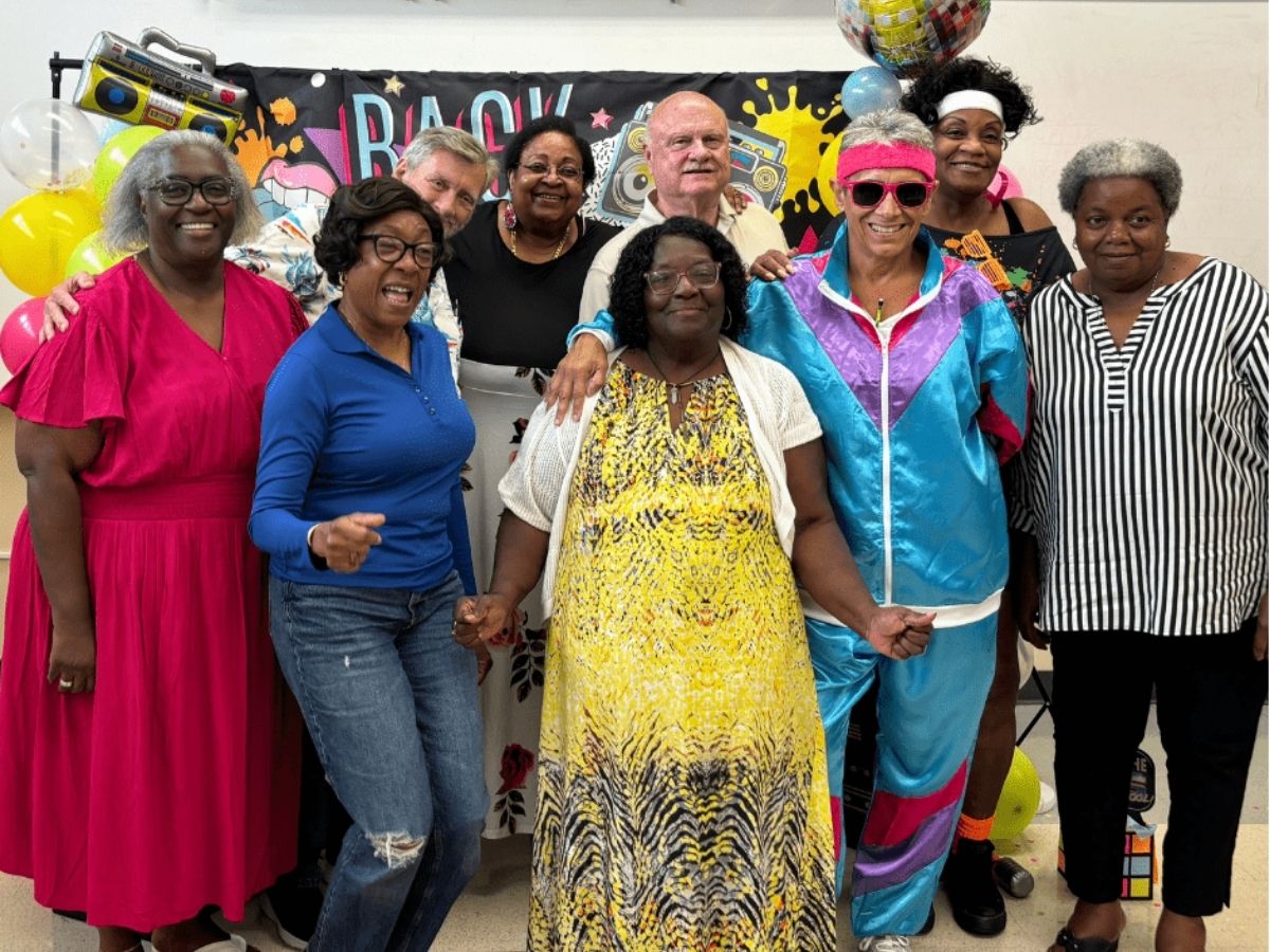 Seniors in Service volunteers pose together in colorful 1980s-themed attire during the organization's 40th anniversary volunteer appreciation celebration.