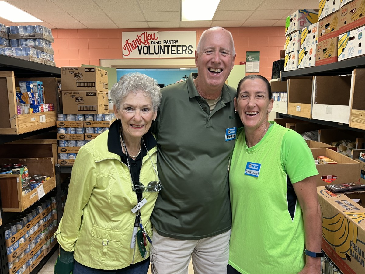 Seniors in Service volunteers smile together while organizing food donations at a Tampa Bay community pantry.