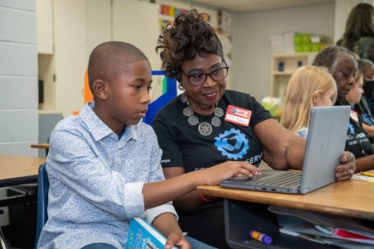 Classroom Grandparent volunteer tutoring student on reading comprehension on computer.