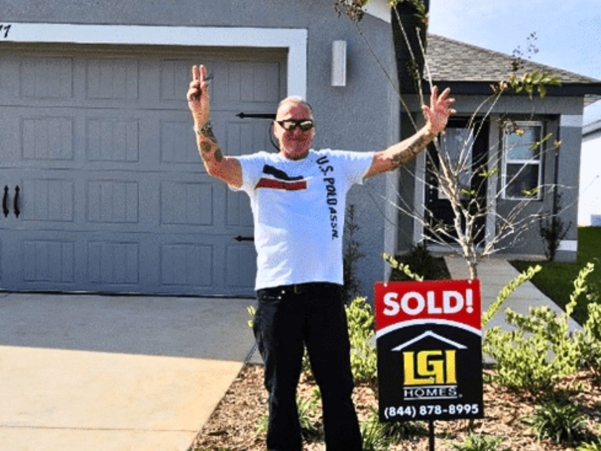 Veteran stands outside his new home beside a sold sign after receiving housing support through Operation: Veteran Connect.