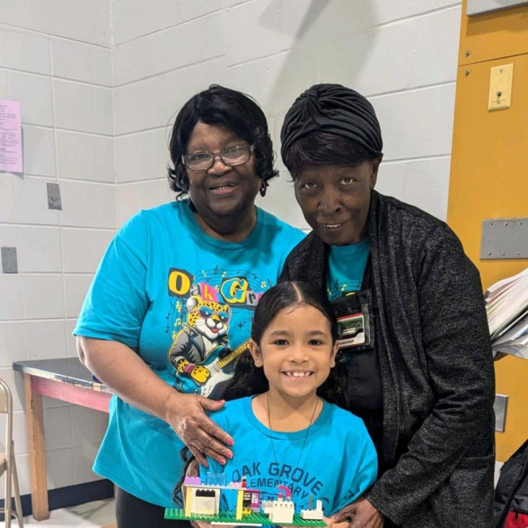 Victoria and Classroom Grandmas Build Meaningful Connections Readers in Motion student Victoria stands with Classroom Grandma volunteers Gladys and Manning during a school learning activity.