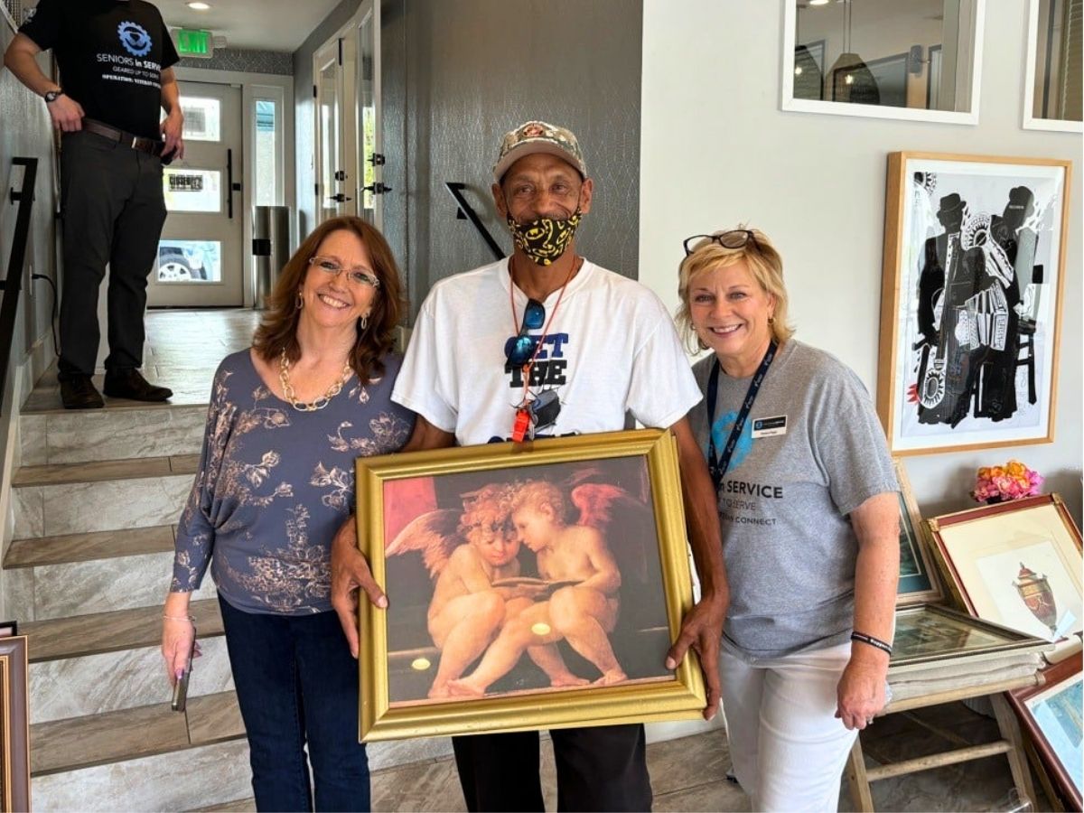 Volunteers help decorate a veteran's new home with donated artwork through the Warm My Walls campaign, creating a welcoming and comfortable living space.